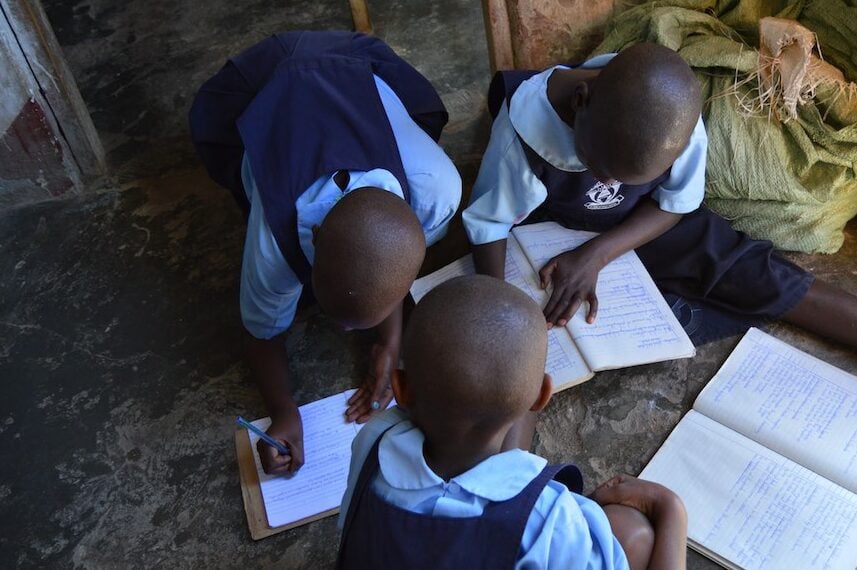 Three pupils work in their school books while sitting on the floor