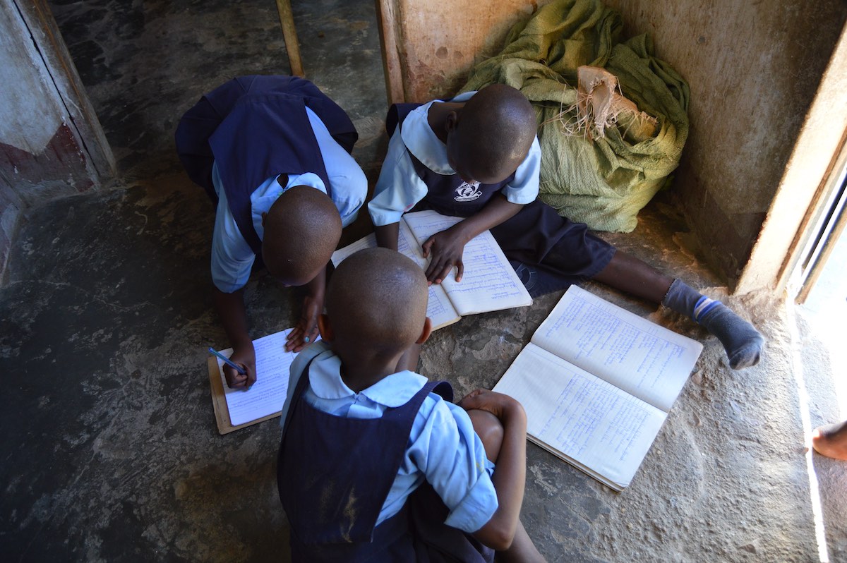 Three pupils work in their school books while sitting on the floor