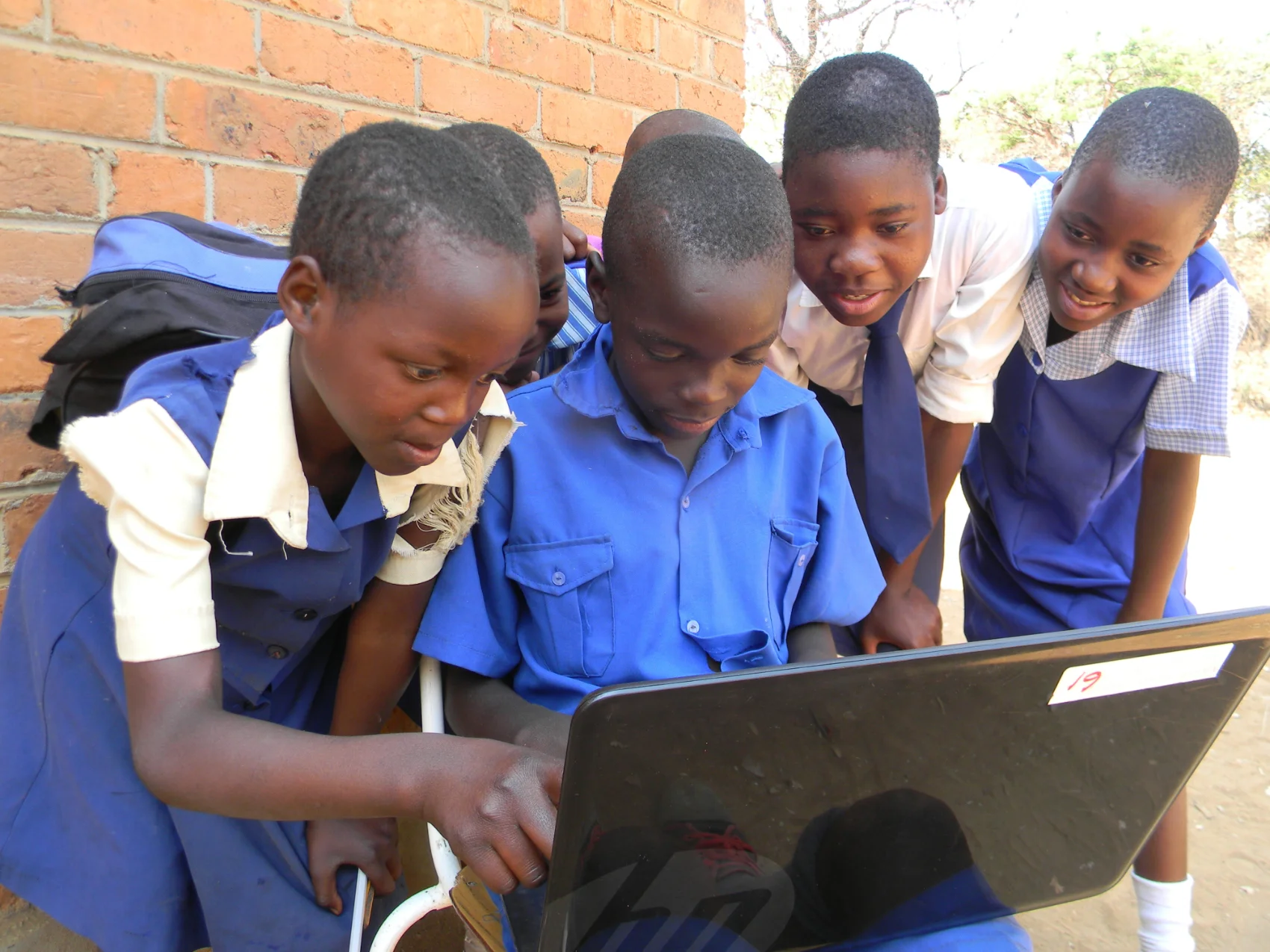 Primary schoolchildren in Africa work together on a laptop outside a school