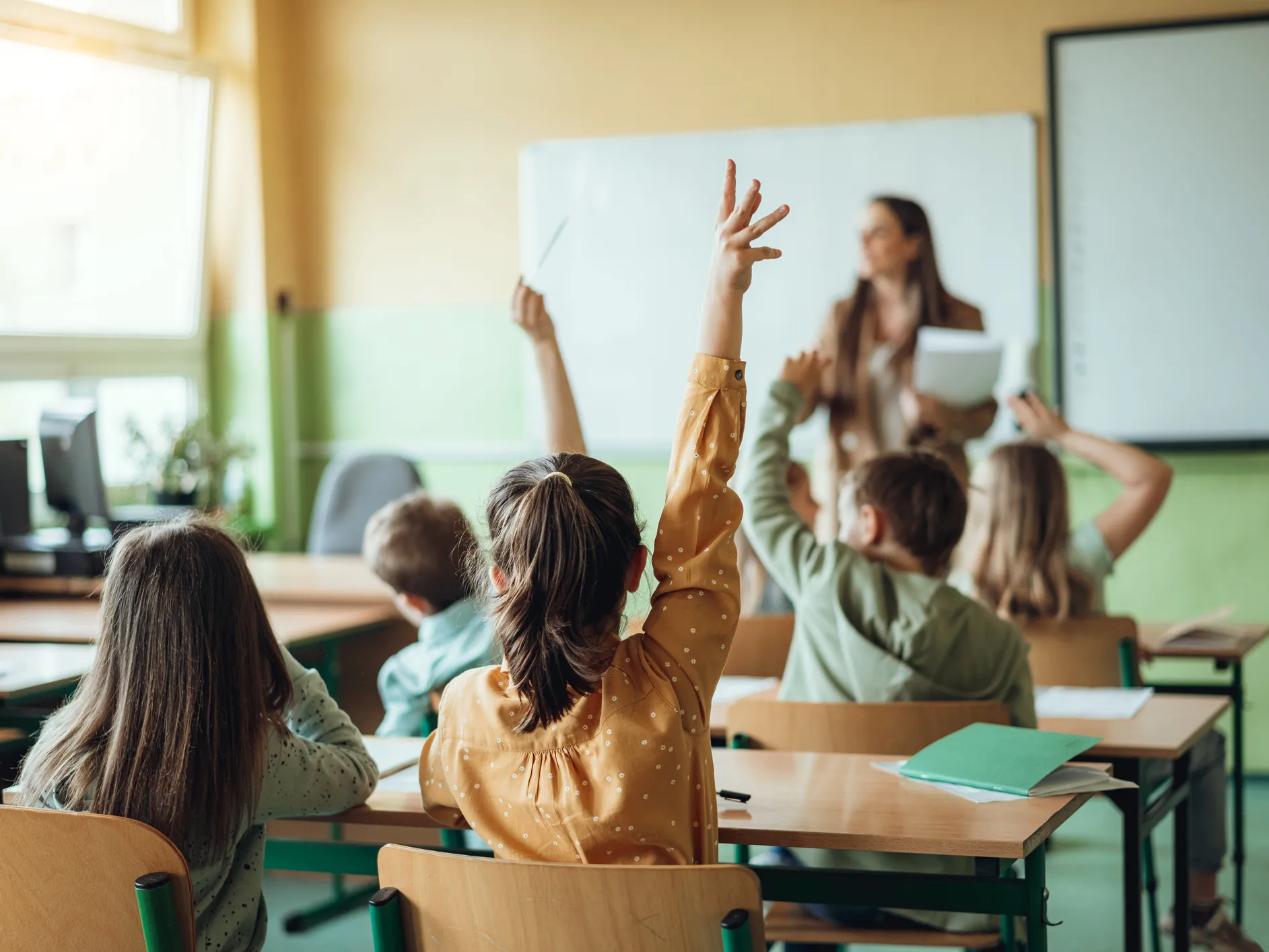 ALT Kids raising the hands to answer a teachers question in a classroom