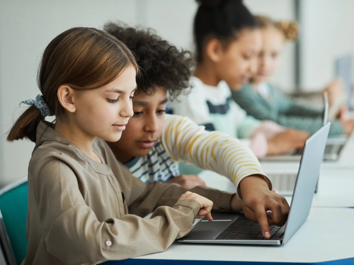 Children work together on a laptop computer in a classroom