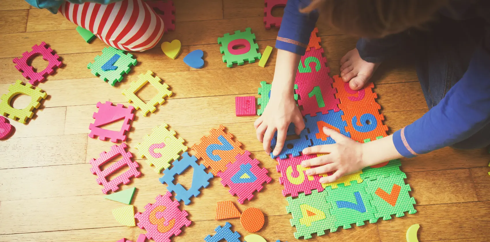 Two young children play with numbered blocks on a wooden floor